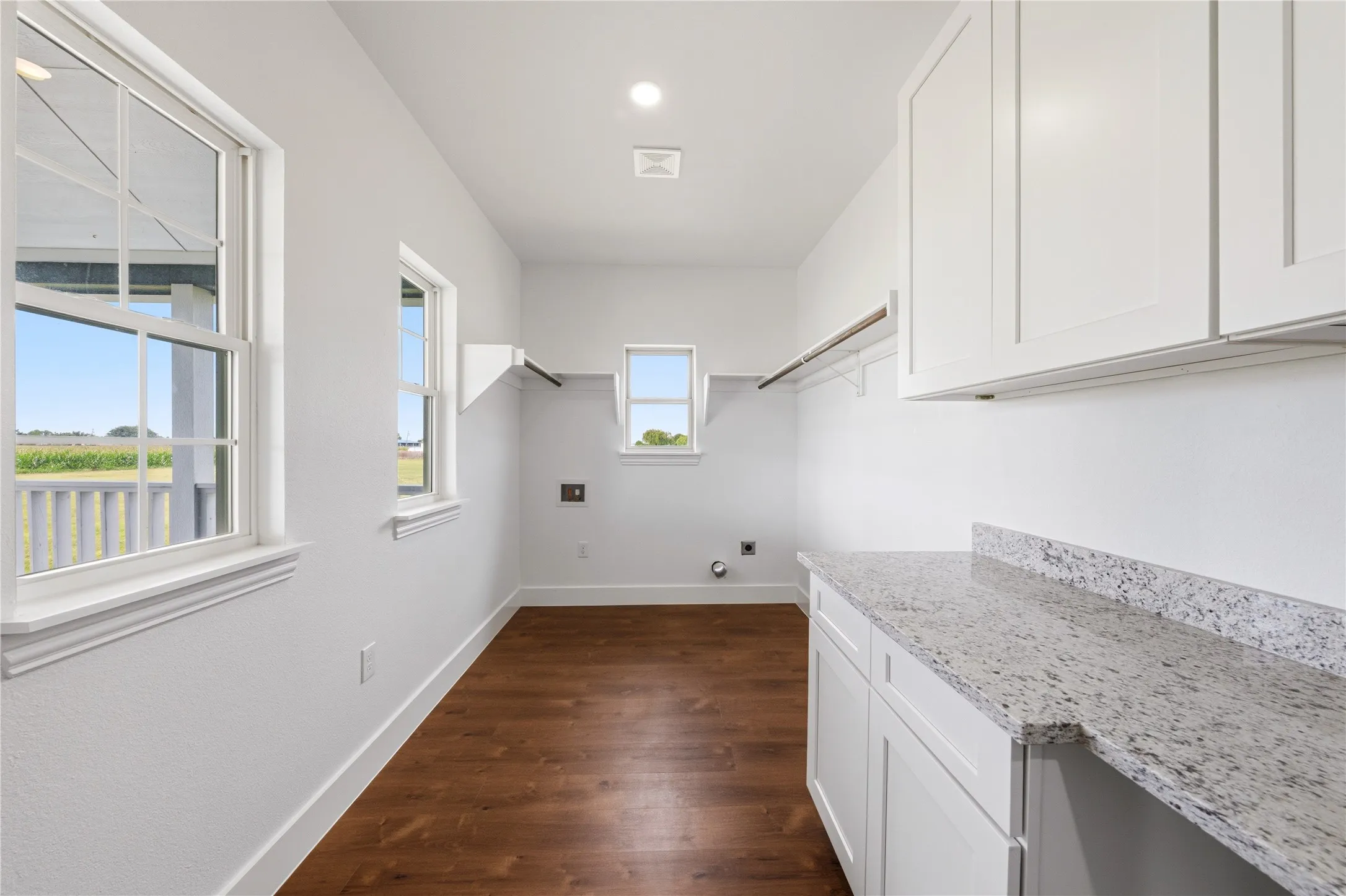 Bright utility space featuring wood-finish flooring, white cabinetry, and a speckled countertop