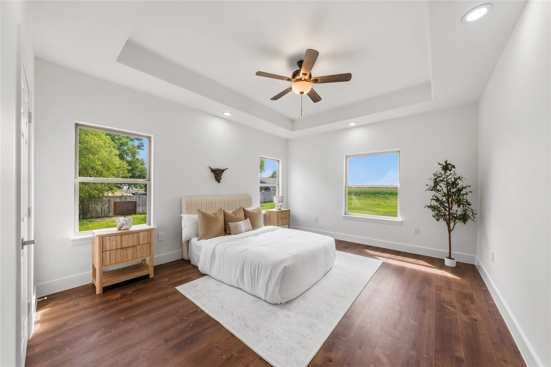 Spacious bedroom featuring a tray ceiling with recessed lighting, wood-finish flooring, and multiple windows