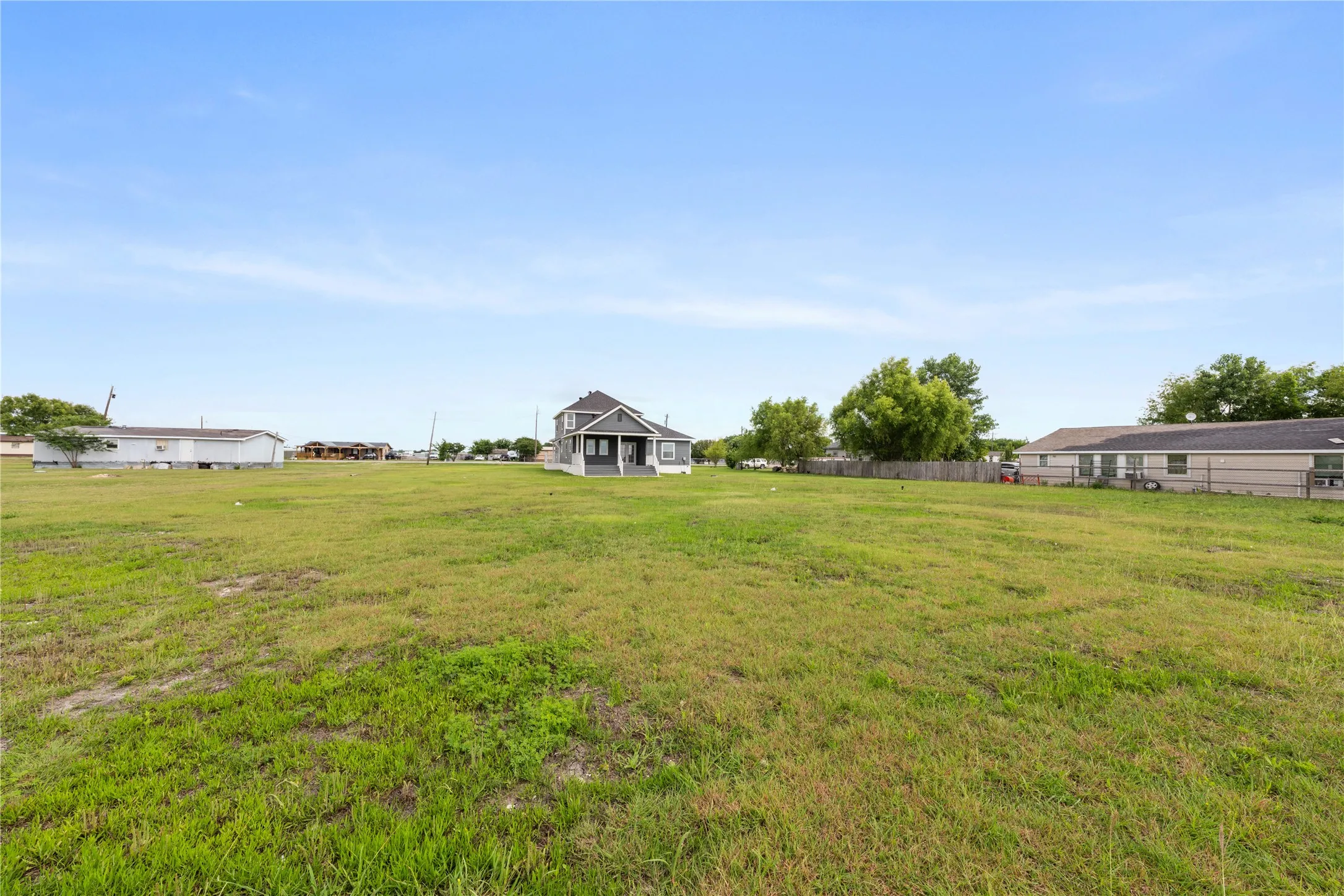 Expansive open lot featuring a central two-story residence with a gray exterior and white trim