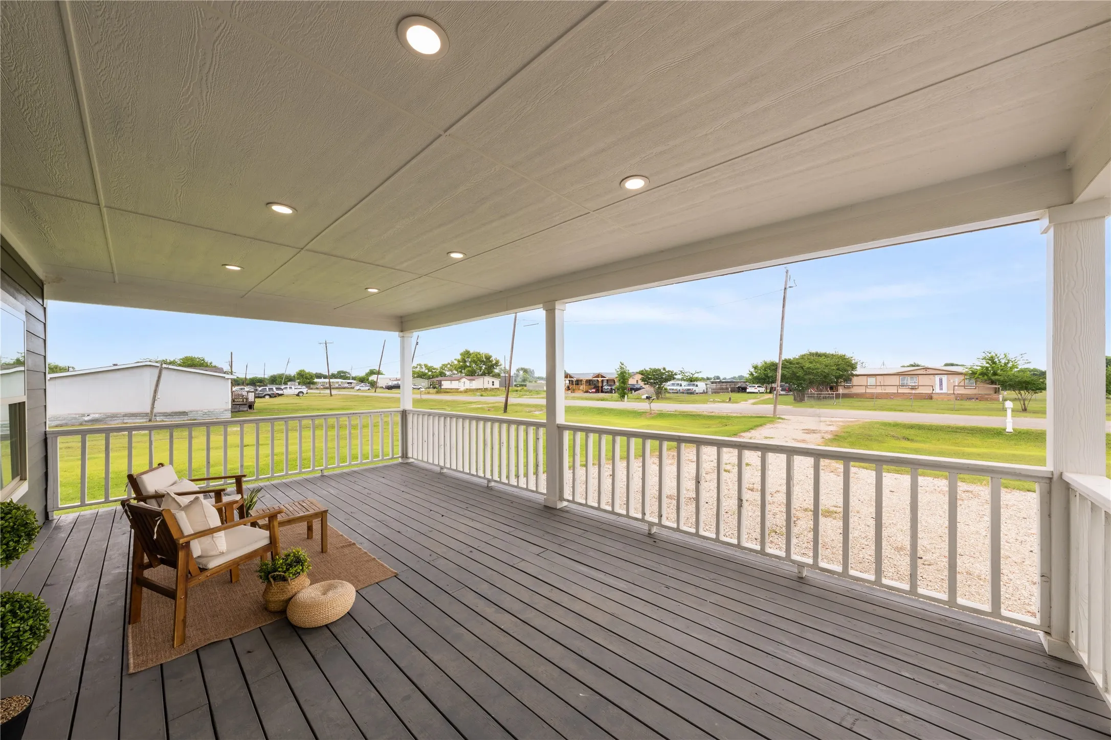 Expansive covered porch featuring grey wood-finish decking, recessed lighting, white railing, and structural support columns