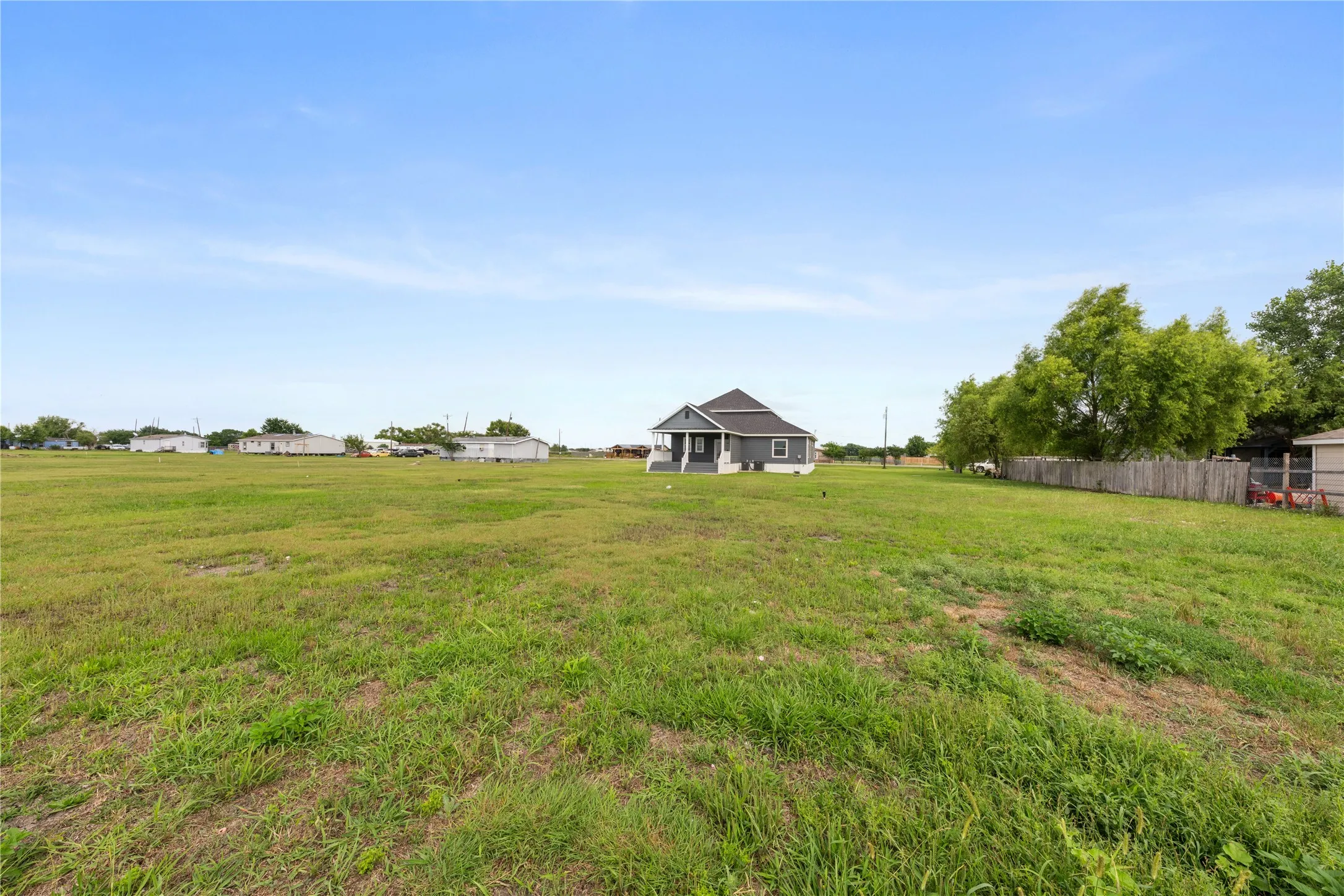 Expansive grassy lot with a detached residence featuring a covered front porch and a dark shingle roof