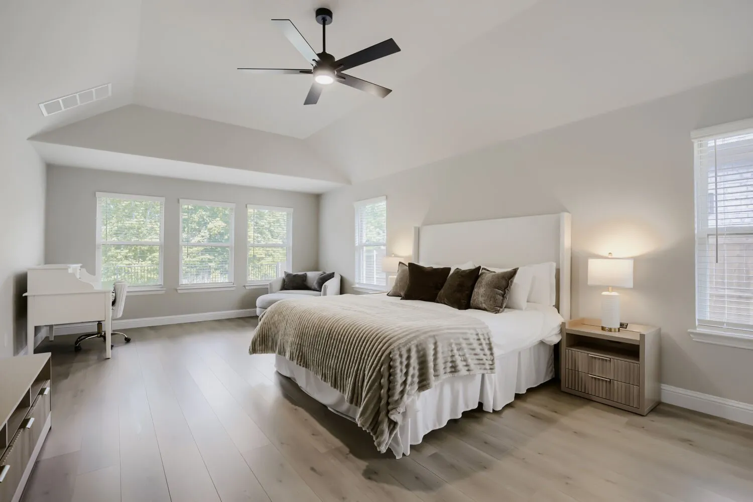 Spacious bedroom featuring vaulted ceilings, light wood-finish flooring, and multiple windows