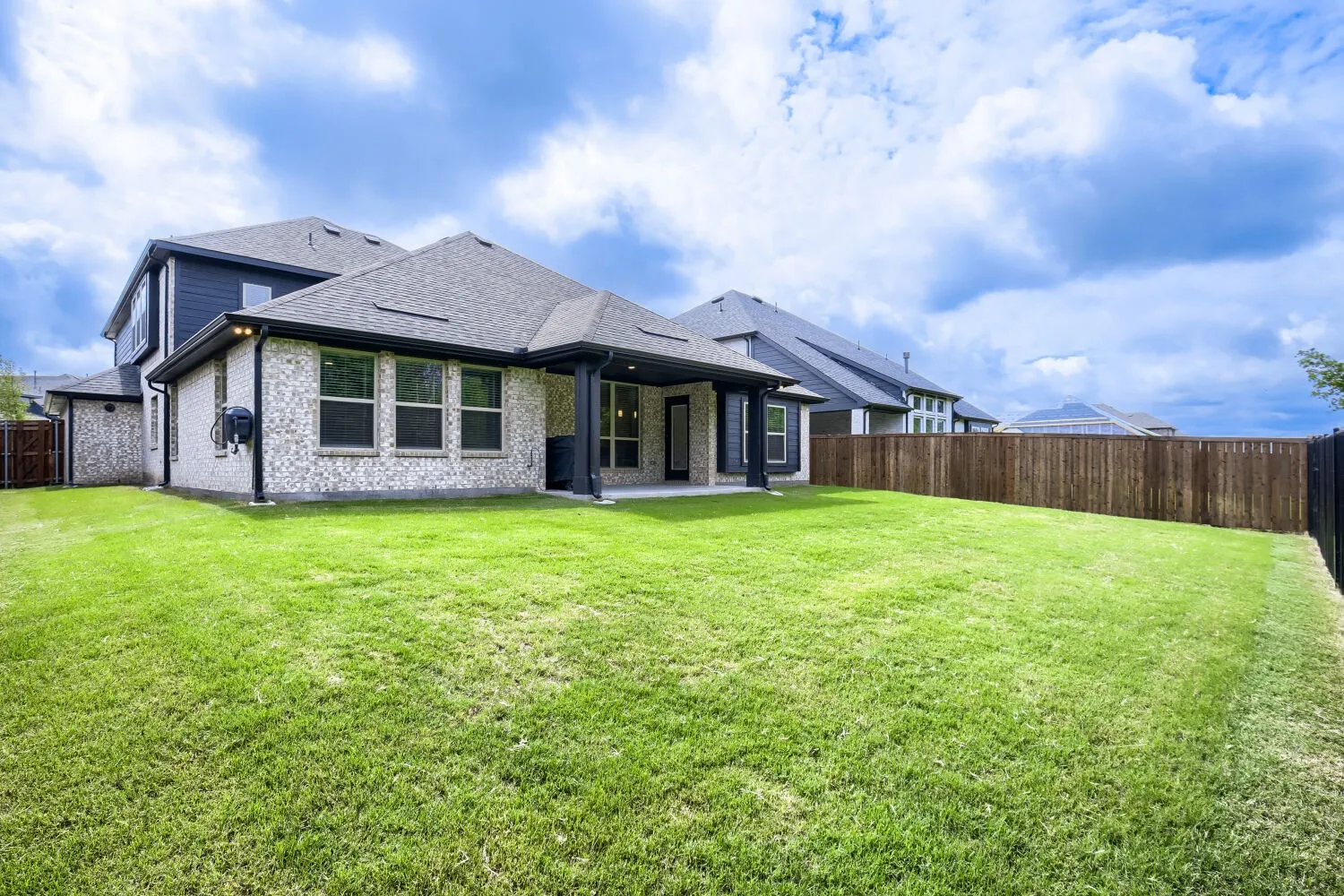 Expansive green lawn with a two-story residence featuring light brick and dark siding