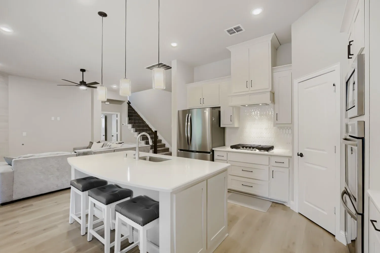 Contemporary kitchen featuring a large island with seating, white shaker cabinetry, stainless steel appliances, and wood-finish​​‌​​​​‌​​‌‌​‌‌​​​‌‌​‌​‌​‌​​​‌​​ flooring
