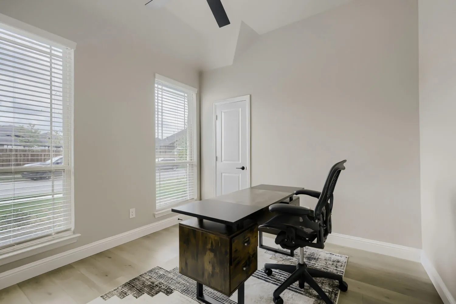 Room featuring two large windows with blinds, light wood-finish flooring, and a vaulted ceiling