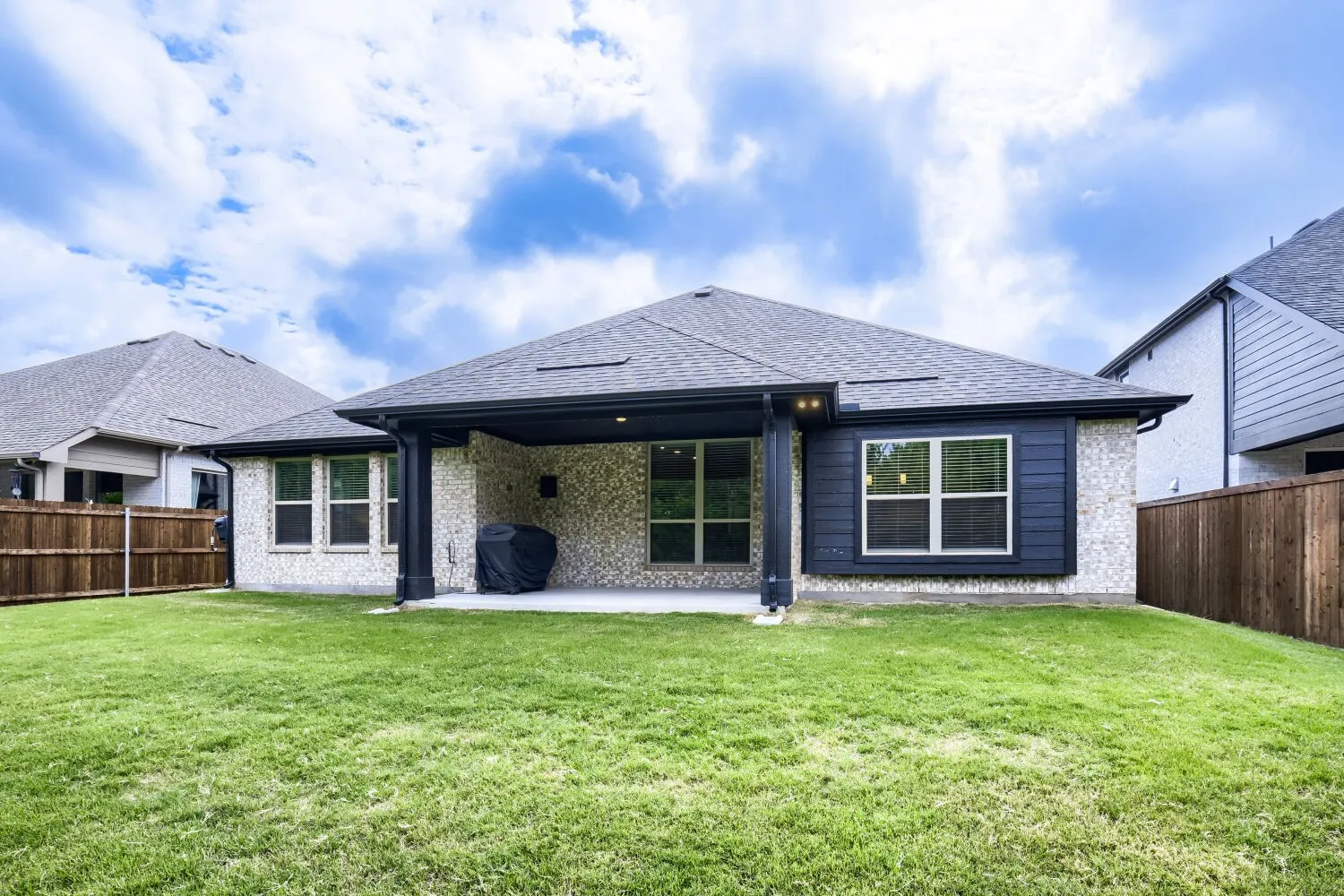 Expansive backyard featuring a manicured lawn, full privacy fencing, and an extended covered patio