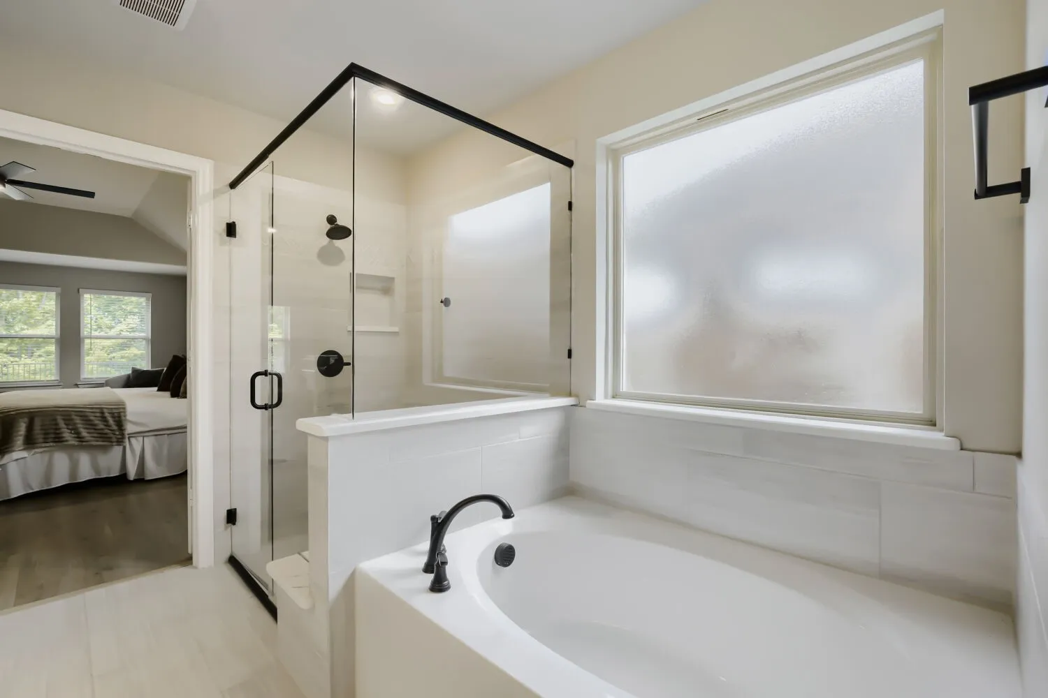 Soaking tub with matte black fixtures, glass-enclosed shower with black trim, frosted window, white subway tile surround, and light-toned wood-finish flooring