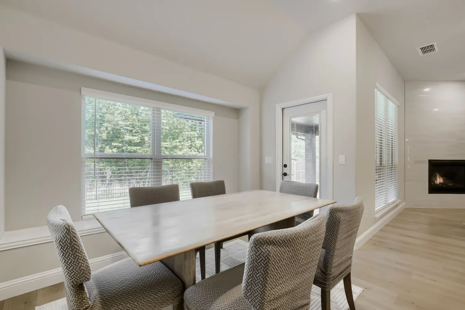 Vaulted ceiling dining area featuring a built-in fireplace, wood-finish flooring, and a glass-paneled exterior door