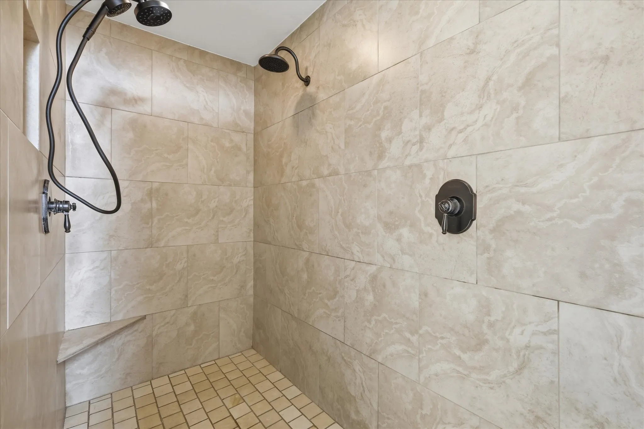 Spacious walk-in shower in primary bath has two shower heads and a seat.
