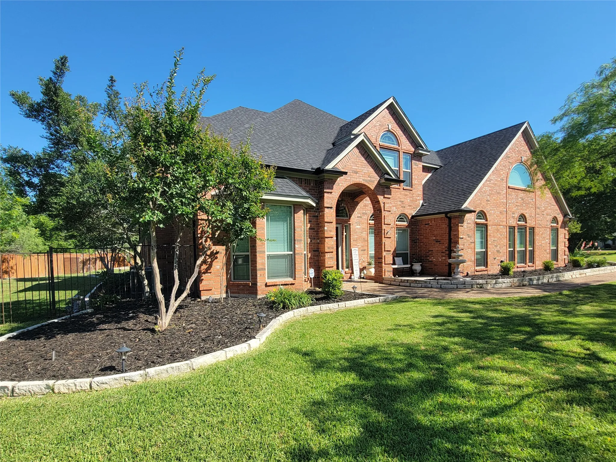 Brick exterior with arched entry, complementing arched windows, and dark shingle roof