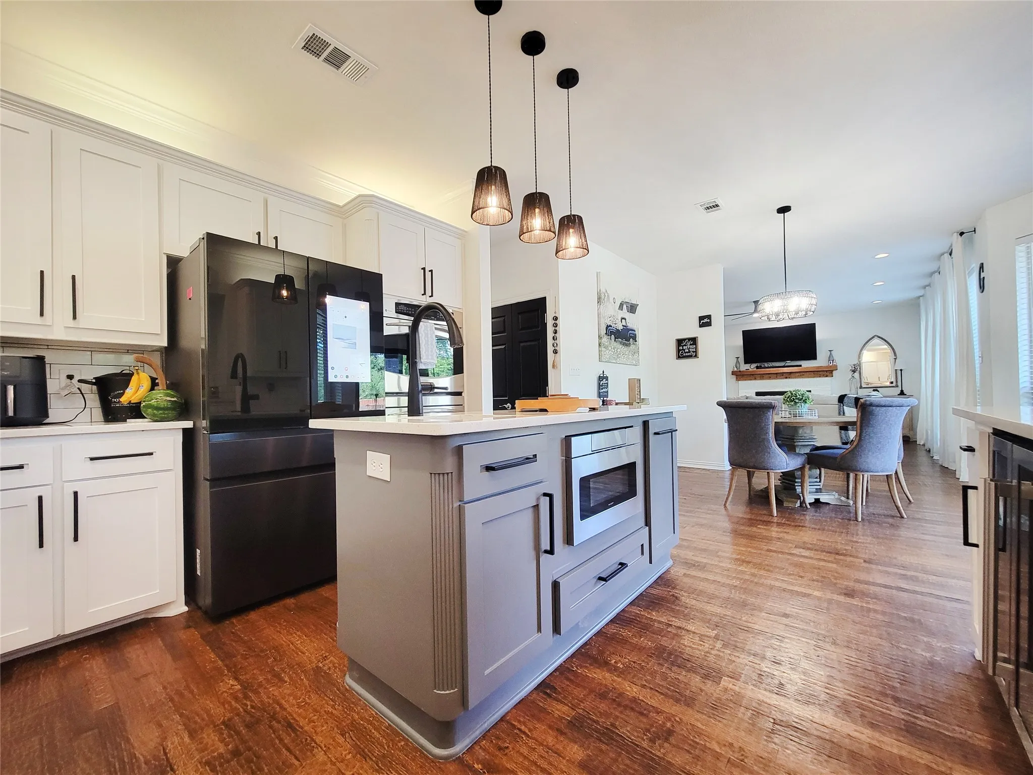 Kitchen featuring a central island with integrated microwave, wood-finish flooring, white cabinetry, and stainless steel appliances