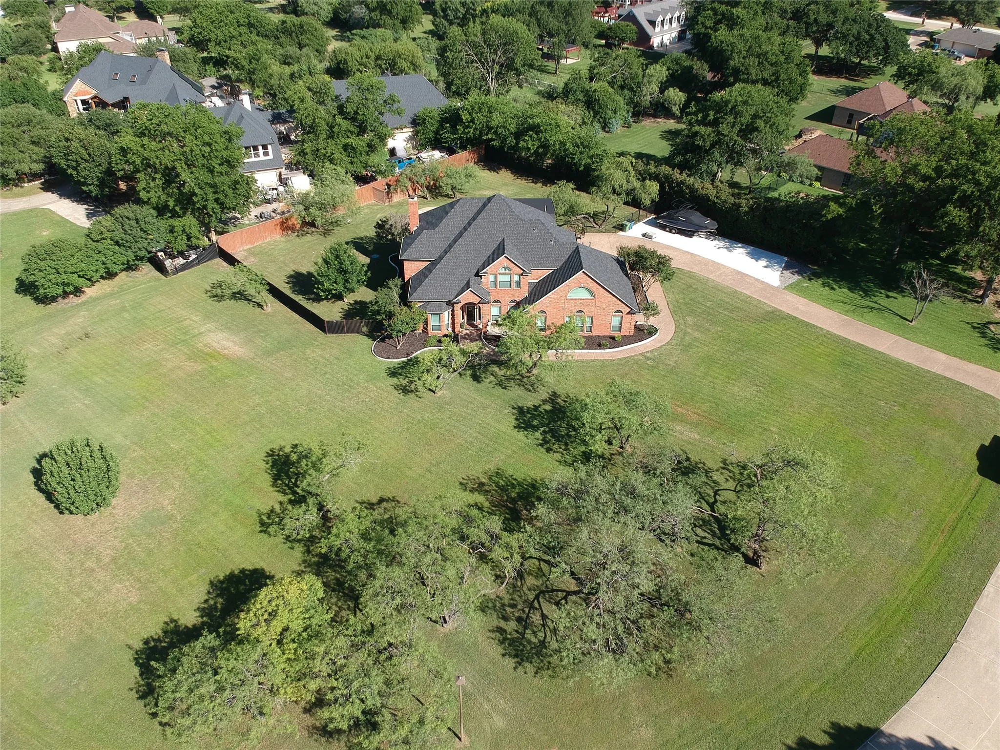 Expansive lot featuring a brick residence with a dark shingle roof, mature trees, and a long driveway