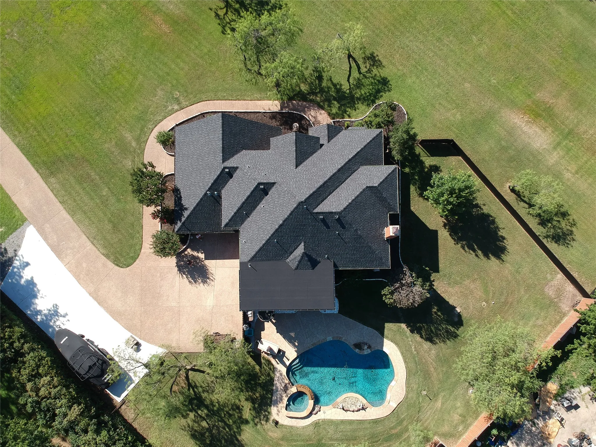 Expansive property featuring a multi-gabled roofline, a large paved driveway, a freeform swimming pool with integrated spa, and extensive green lawn areas