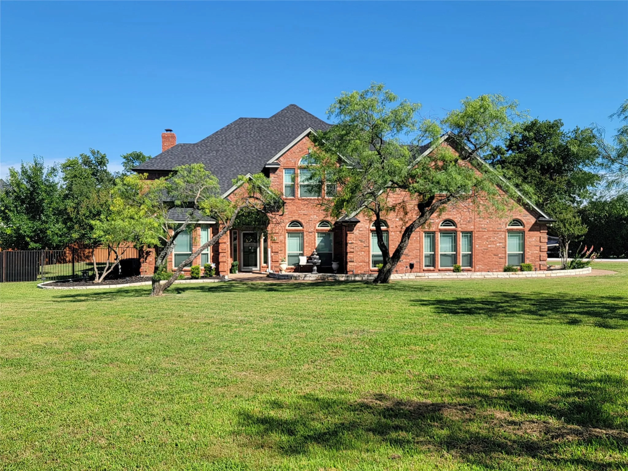 Traditional red brick exterior featuring a dark shingle roof, arched windows, and a manicured front lawn