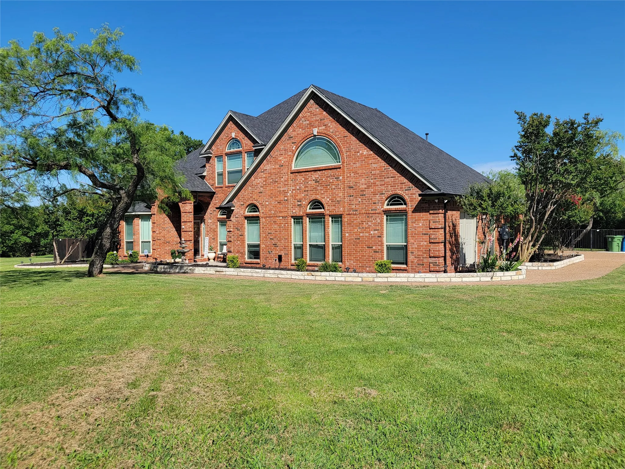 Red brick exterior with arched windows, a dark shingle roof, and a stone-edged landscape bed
