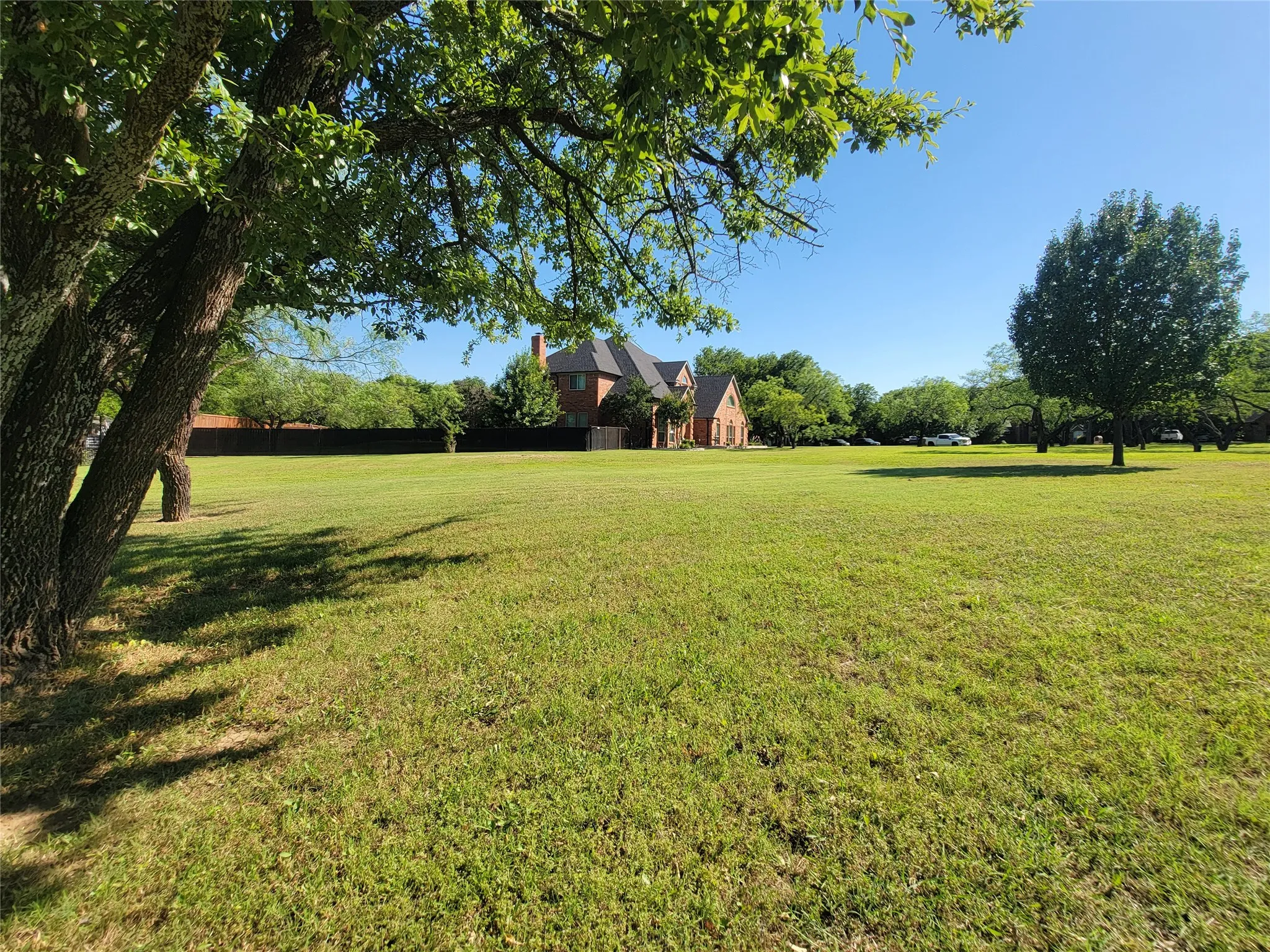 Expansive green space featuring mature trees and a distant brick residence