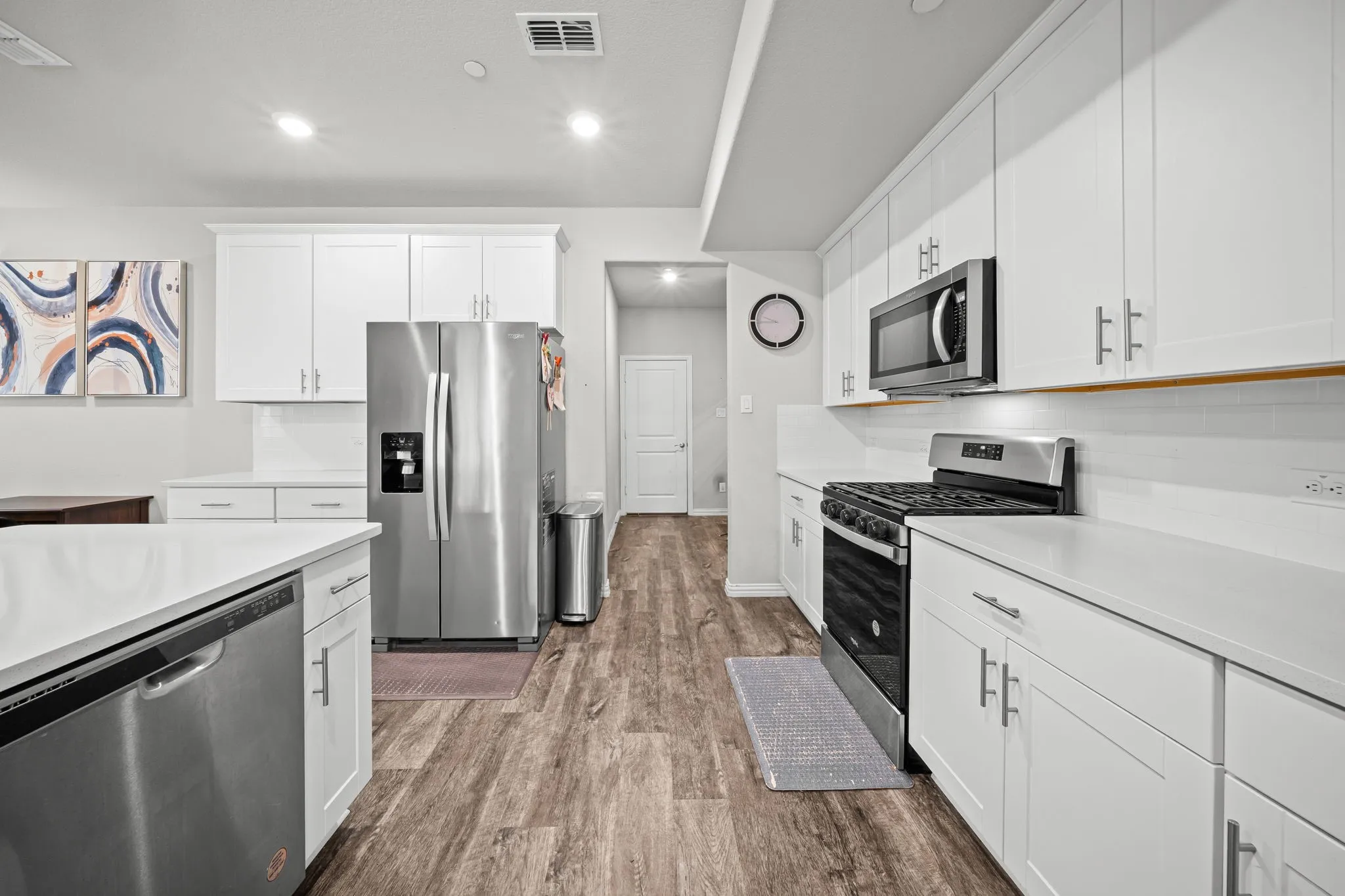 Kitchen featuring white shaker-style cabinetry, stainless steel appliances, solid surface countertops, and wood-finish flooring