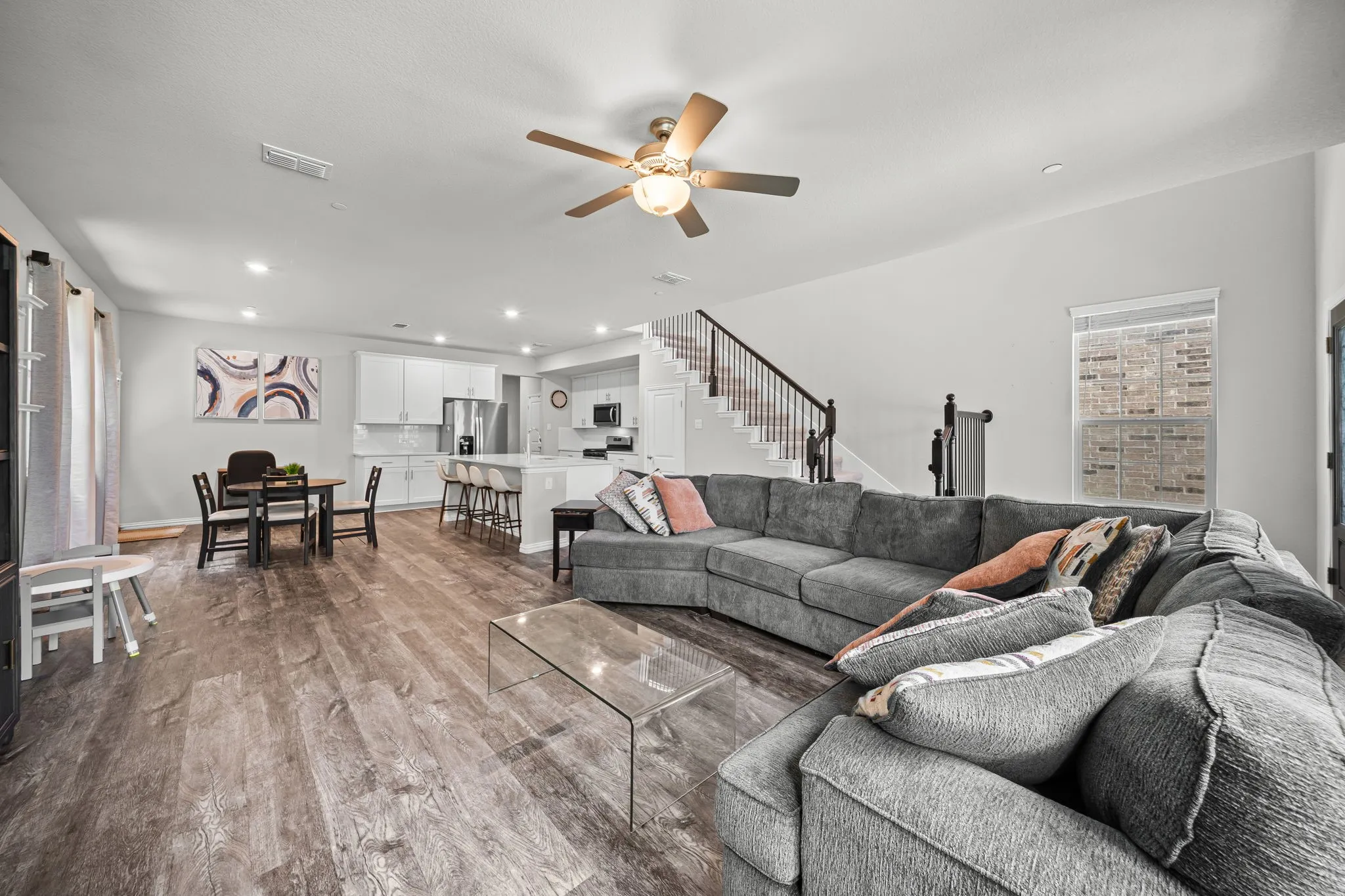 Open-concept living space featuring wood-finish flooring, recessed lighting, a ceiling fan, and a staircase with dark wood railings