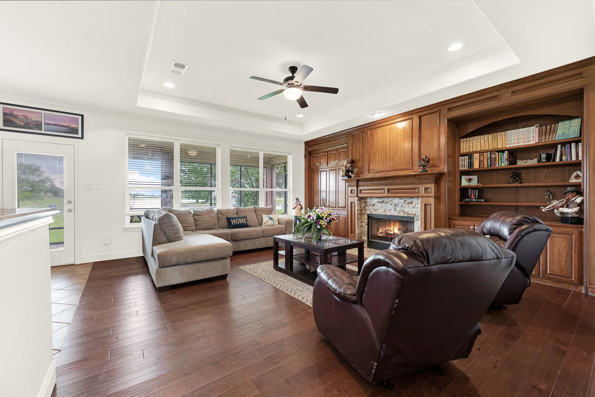 Living area featuring wood-finish flooring, a tray ceiling with recessed lighting, and a ceiling fan