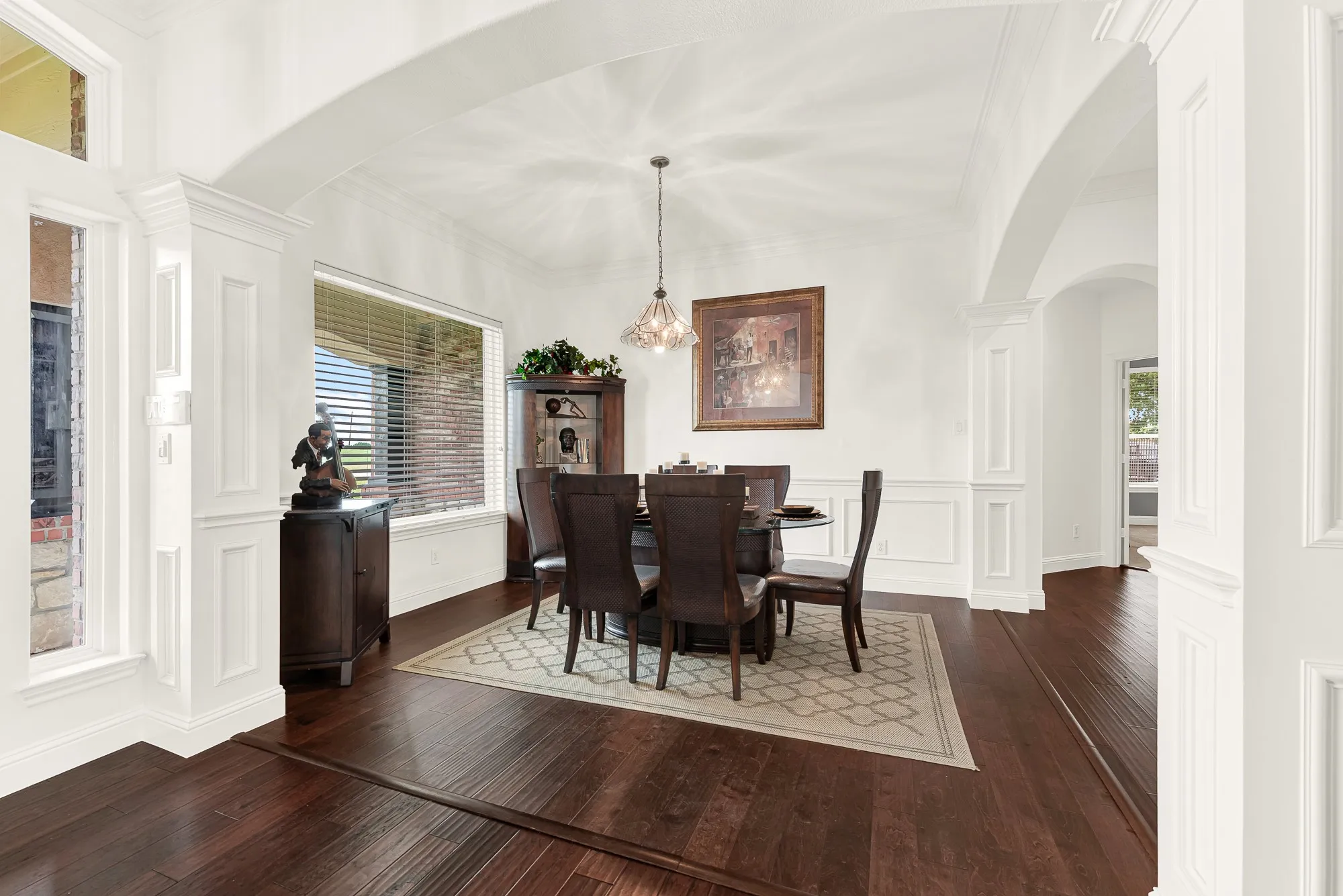 Formal dining area featuring dark wood-finish flooring, architectural archways, and wainscoting