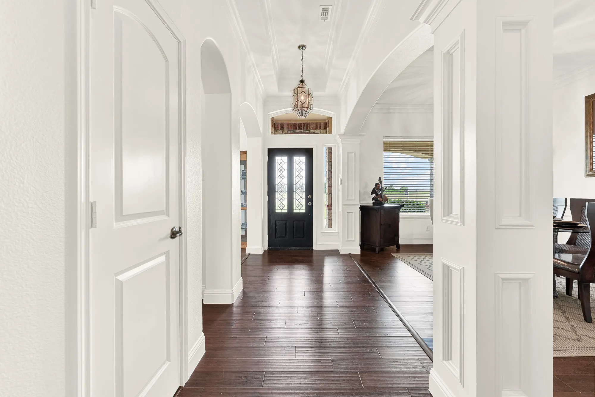 Enter Custom Luxury Foyer featuring dark wood-finish flooring, custom doors, archways, coffered ceiling, and a decorative pendant light fixture