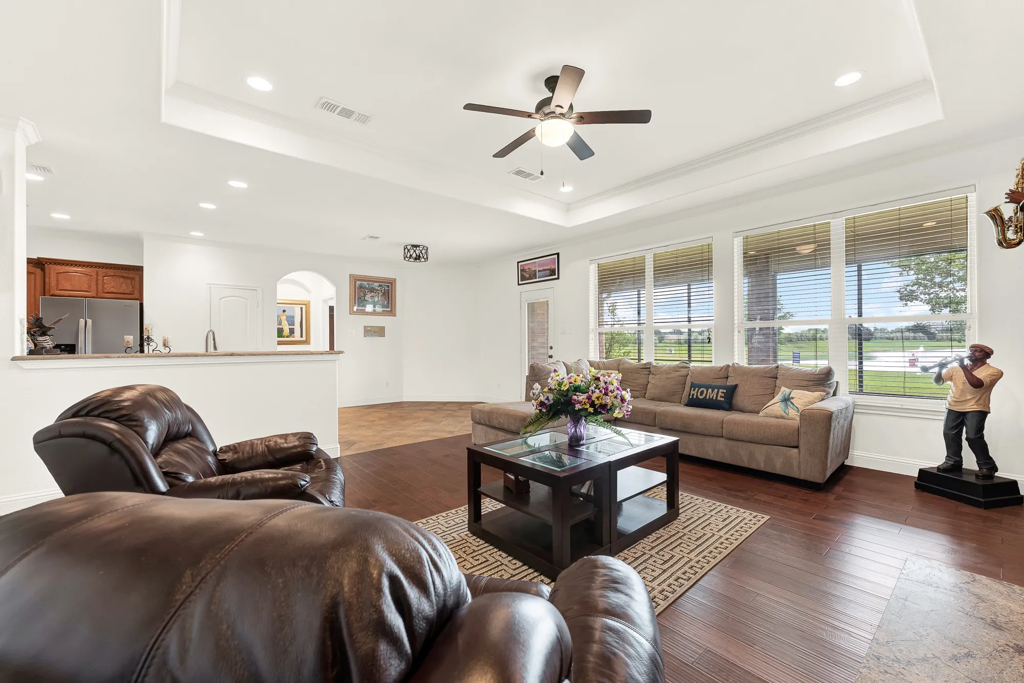 Spacious living area featuring dark wood-finish flooring, a tray ceiling with a ceiling fan, and recessed lighting