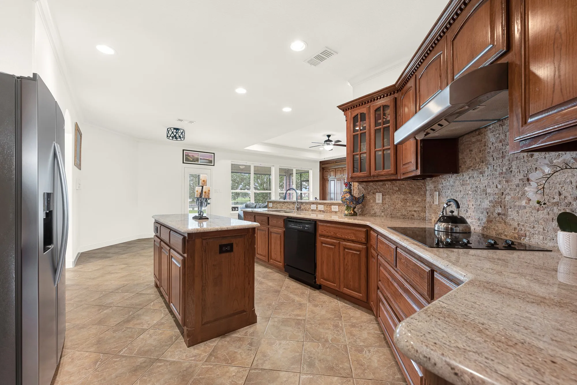 Kitchen featuring wood cabinetry, stone countertops, a tile backsplash, and a central island with additional storage