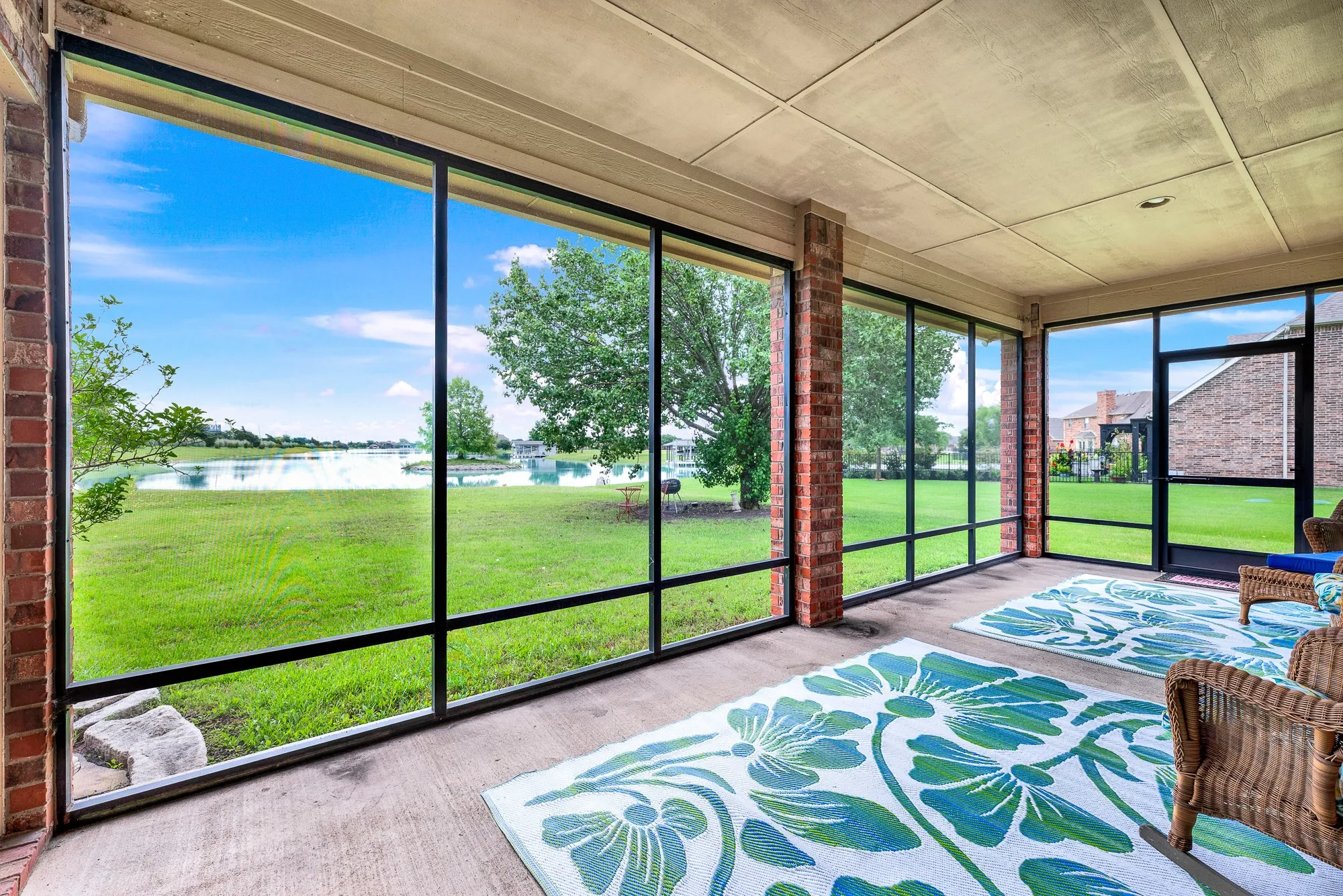 Screened porch featuring extensive window panels, brick pillars, concrete flooring, and a paneled ceiling