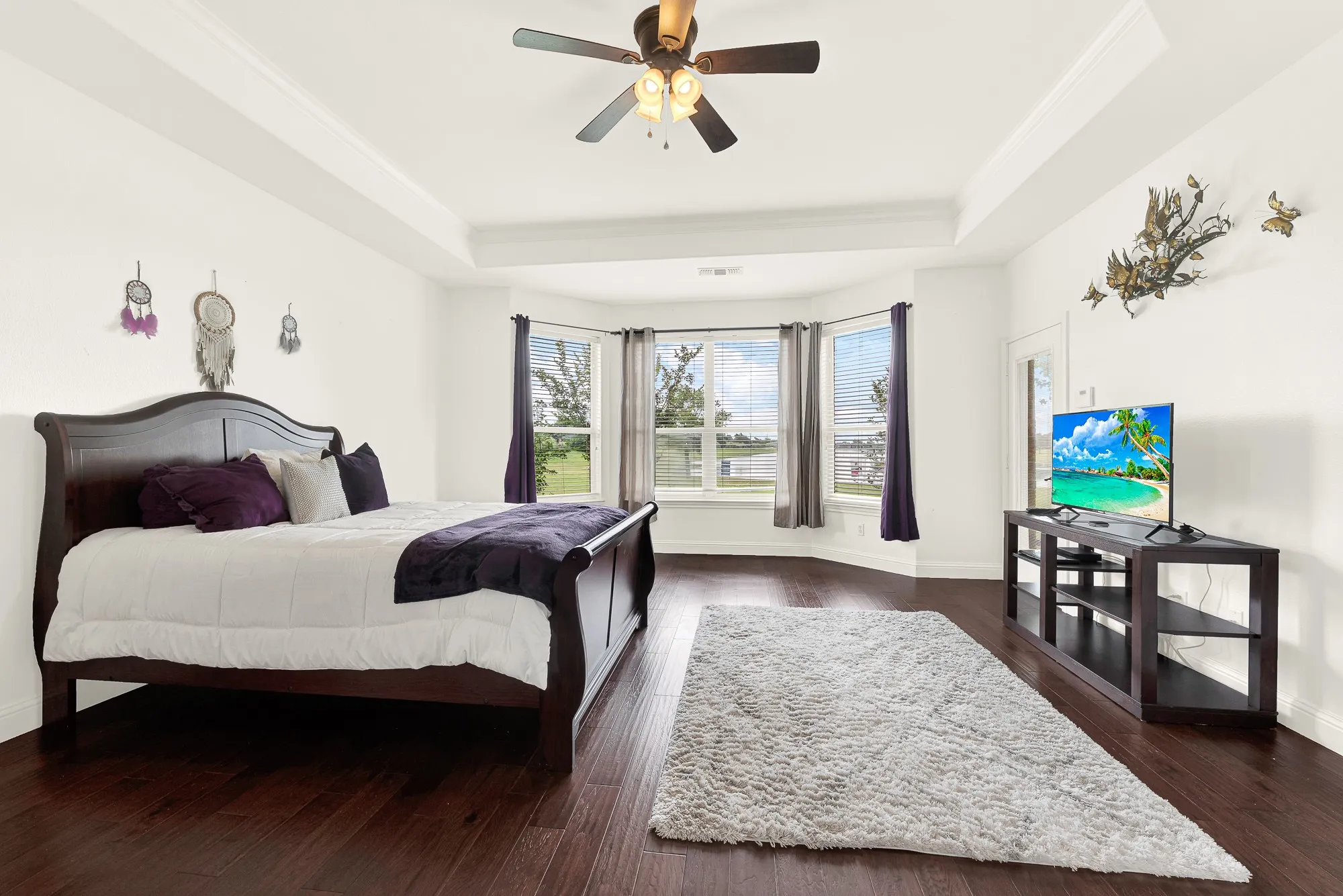 Primary Suite with lake view. Spacious room with GREAT view of lake, featuring rich wood-finish flooring and a tray ceiling with a ceiling fan