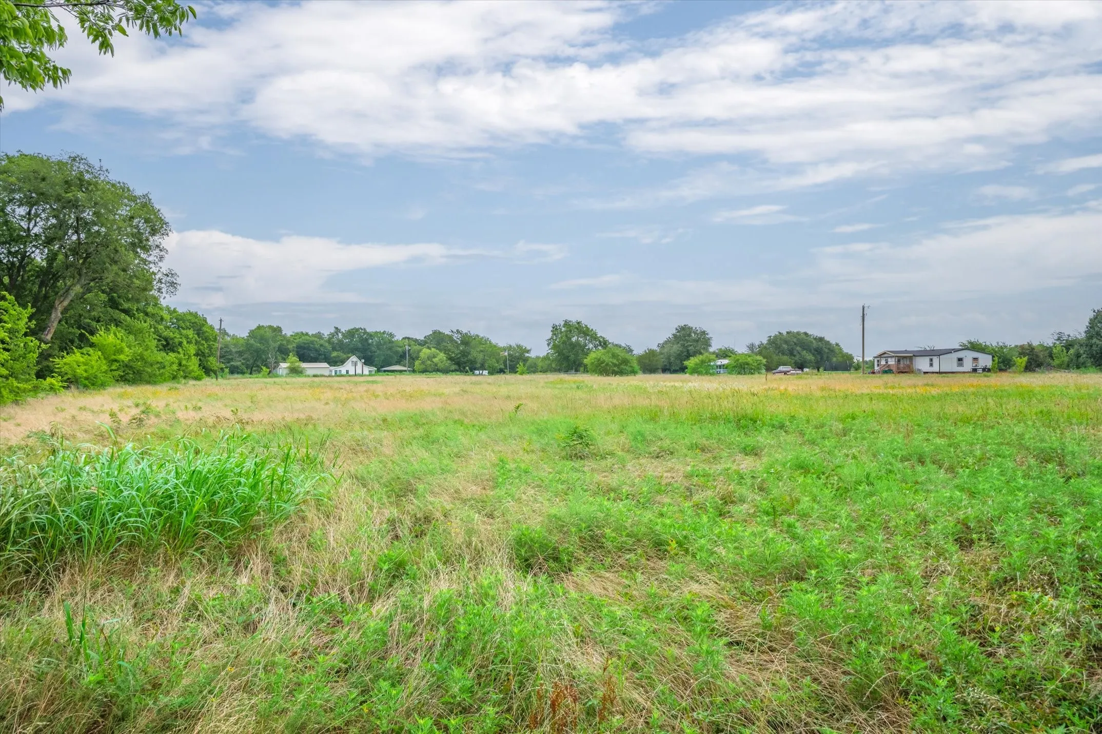 Side aerial view looking for the east to west. Pasture in front, house in the trees in middle and pond at the back