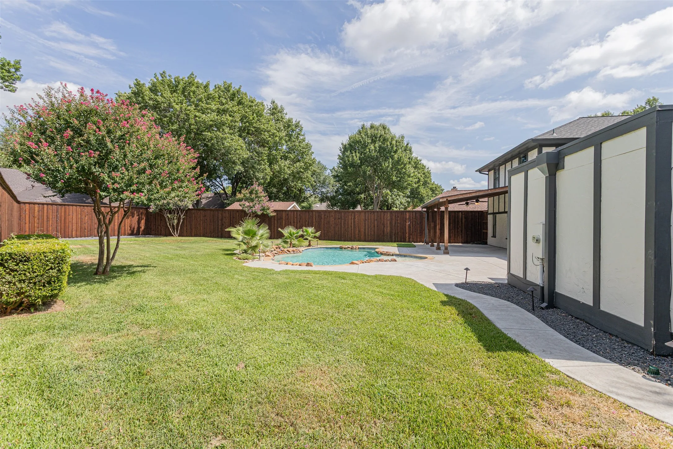 Wide backyard perspective showcasing pool, patio, and mature trees.