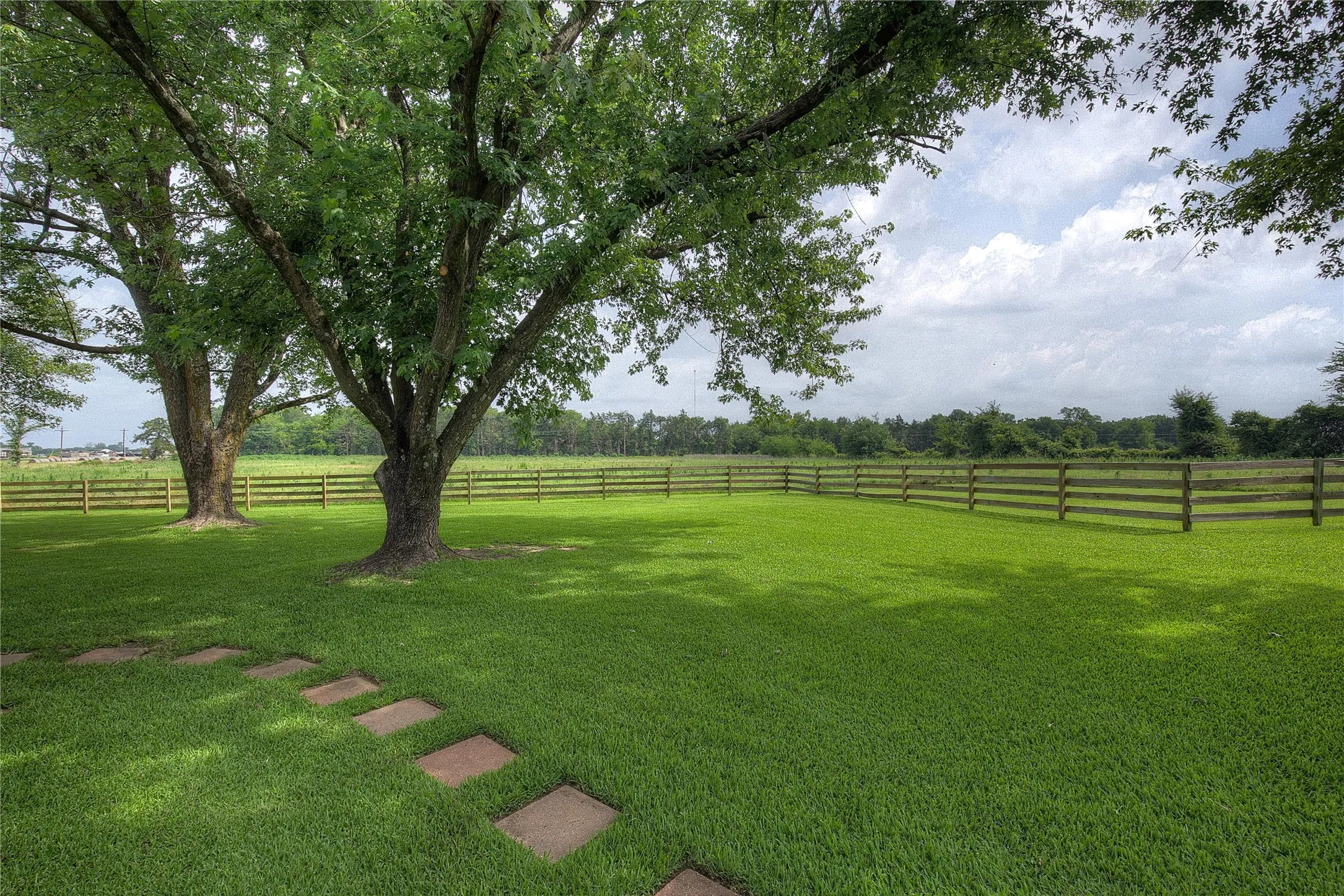 The house sits on a manicured acre of St. Augustine grass; wood fence separates you from the ag-exempt acreage beyond.