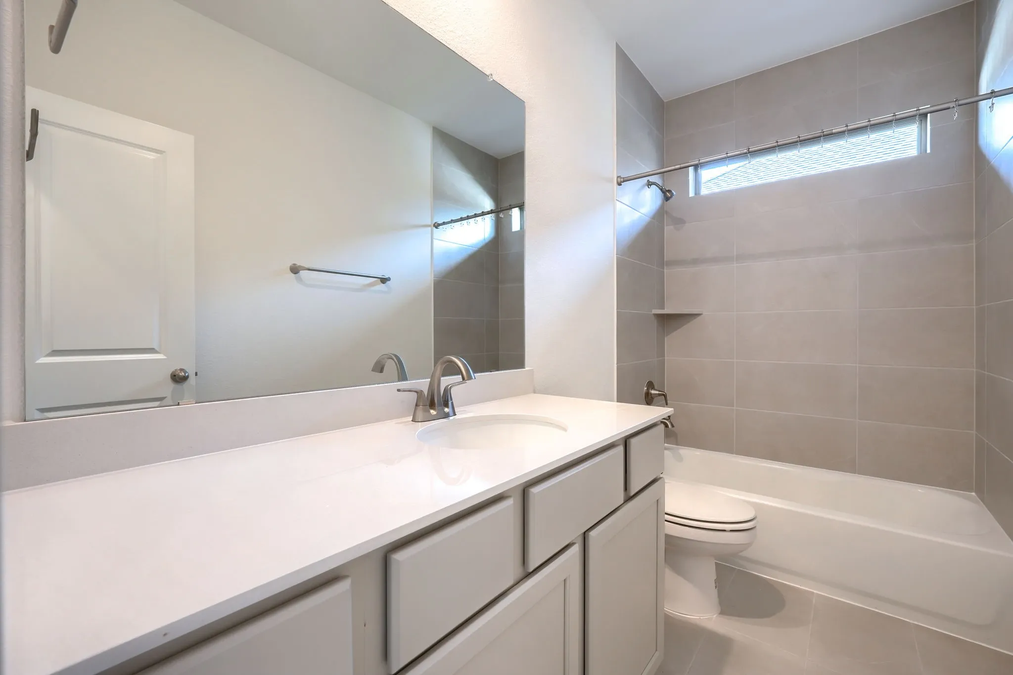 Bathroom featuring a vanity with a white countertop and undermount sink, brushed nickel faucet, full-width mirror, and a tub/shower combination with tile surround and built-in shelf