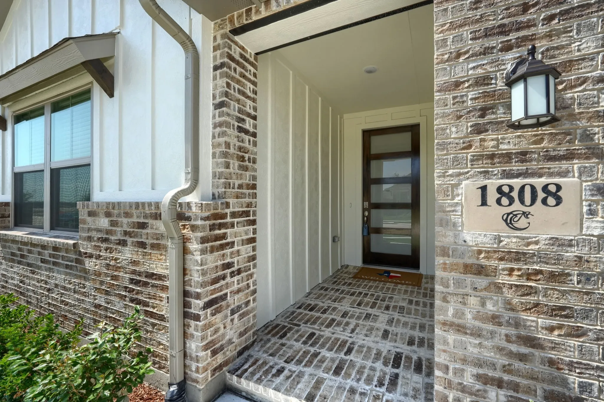 Brick and board-and-batten exterior featuring a modern front door with frosted glass panels