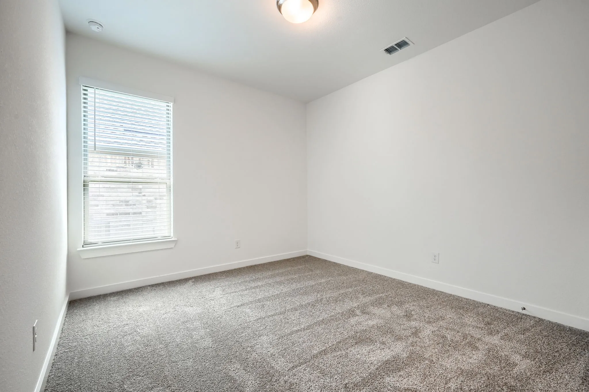 Bright interior room featuring neutral-toned carpet, white walls, and a window with blinds