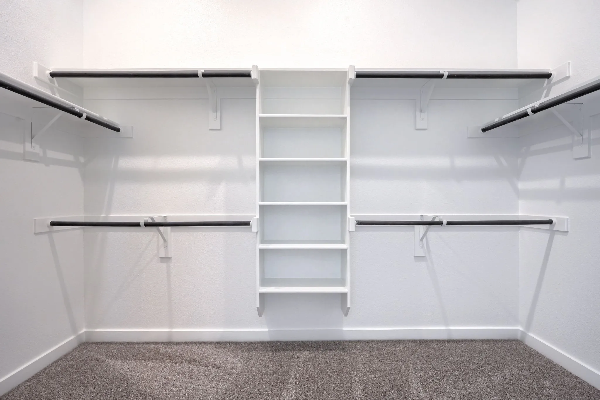 Spacious closet featuring built-in shelving, multiple hanging rods, white walls, white baseboards, and carpet flooring