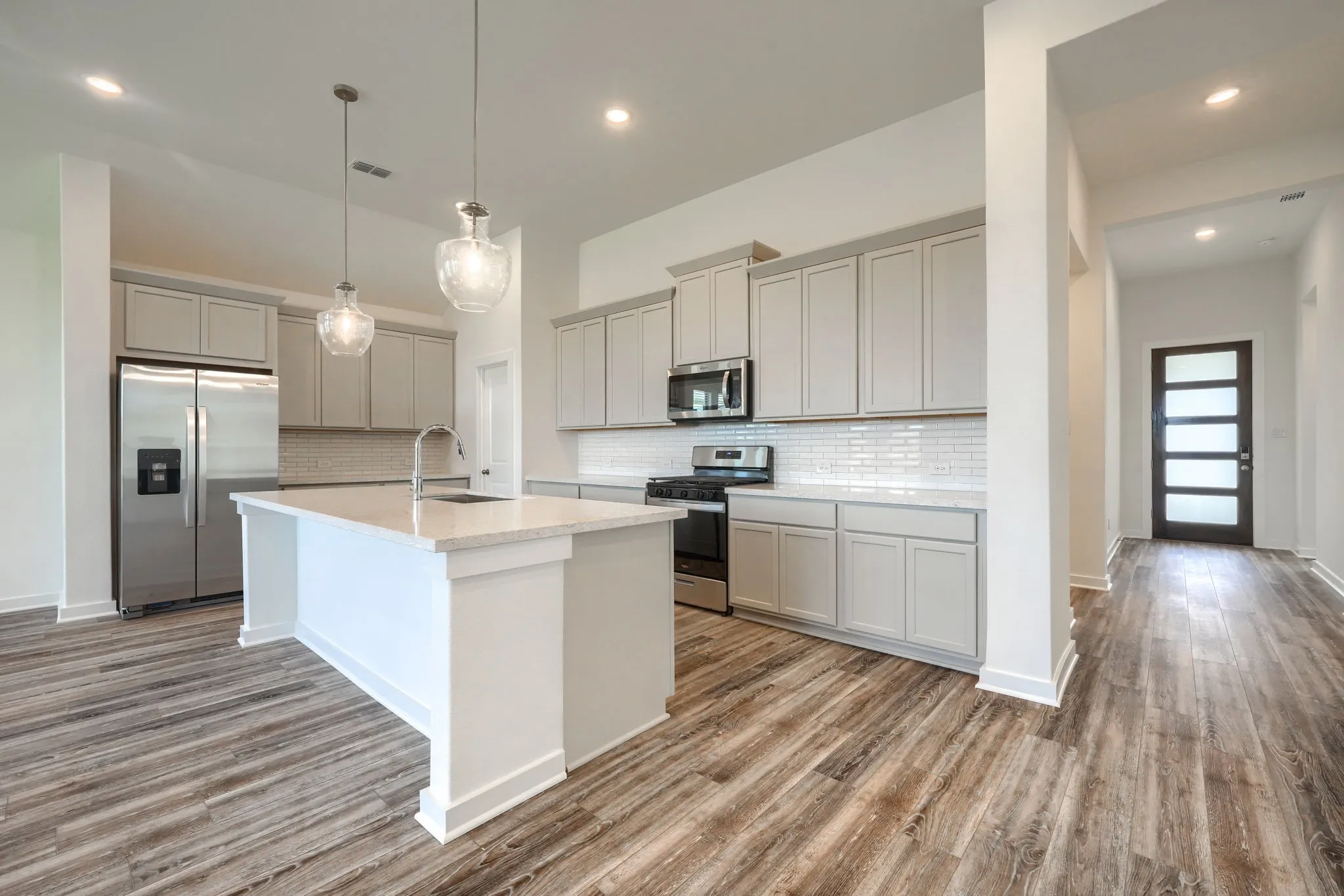 Modern kitchen featuring a central island with a sink, quartz countertops, stainless steel appliances, and wood-finish flooring