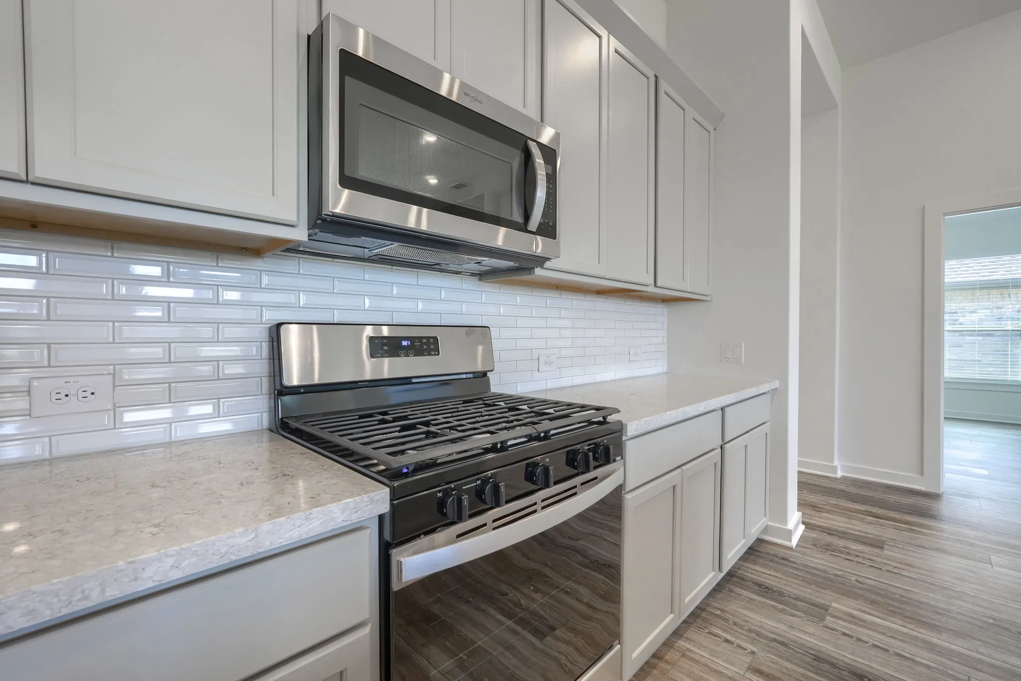 Kitchen featuring stainless steel range with gas cooktop, built-in microwave, light gray cabinetry, subway tile backsplash, and light-toned countertops
