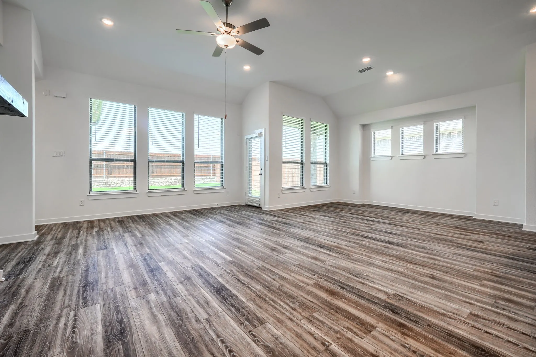 Spacious room featuring wood-finish flooring, abundant natural light from multiple windows, recessed lighting, a ceiling fan, and a vaulted ceiling