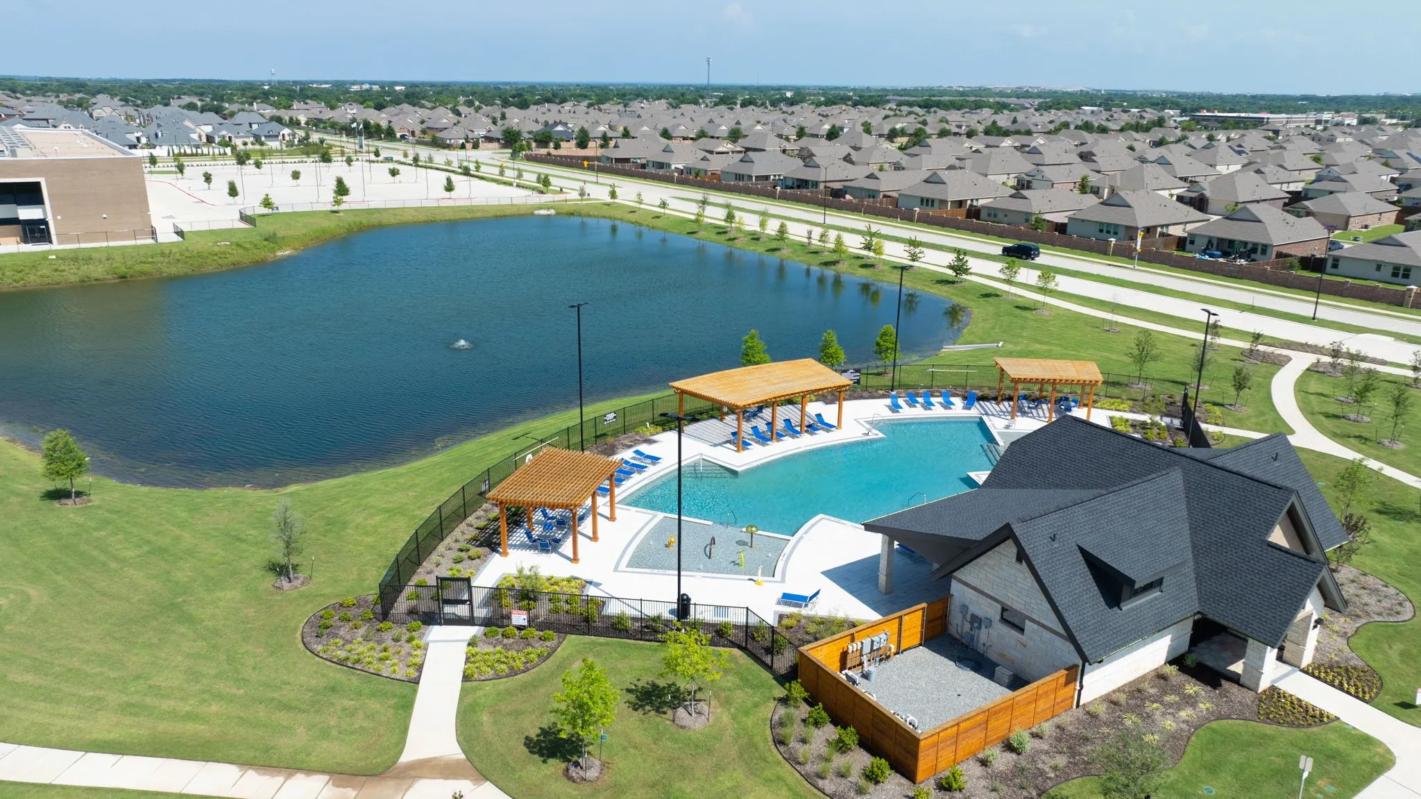 Community amenity center featuring a multi-level swimming pool, two covered pergolas, and an adjacent building with a dark shingle roof