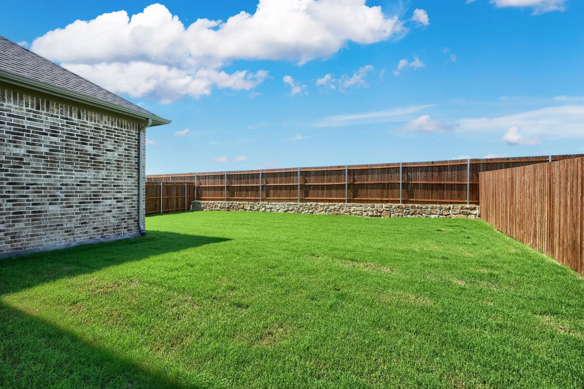 Spacious backyard featuring a manicured lawn, a full wood privacy fence, and a stone retaining wall