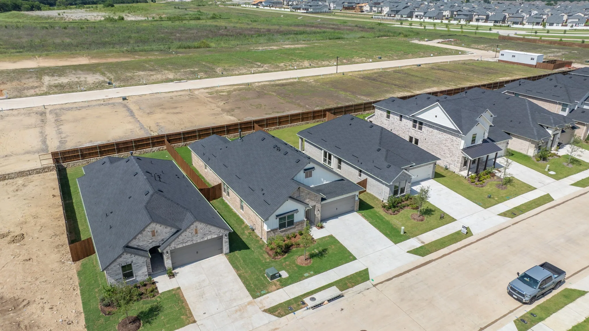 Residential streetscape featuring a row of single-family homes with dark shingle roofs, paved driveways, and landscaped front yards