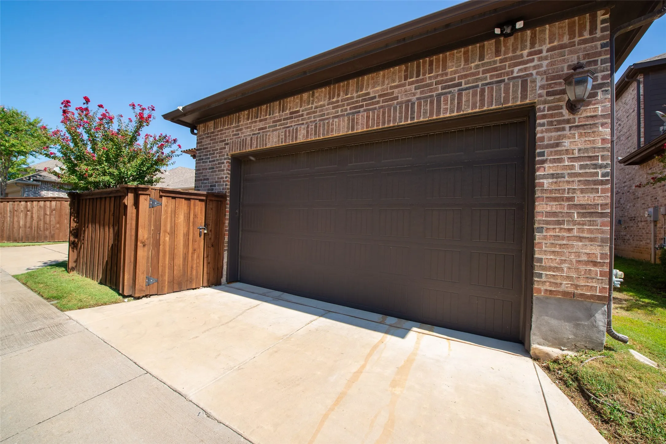 Brown panel garage door with a brick facade featuring a wall-mounted light fixture and dual motion-sensor lighting