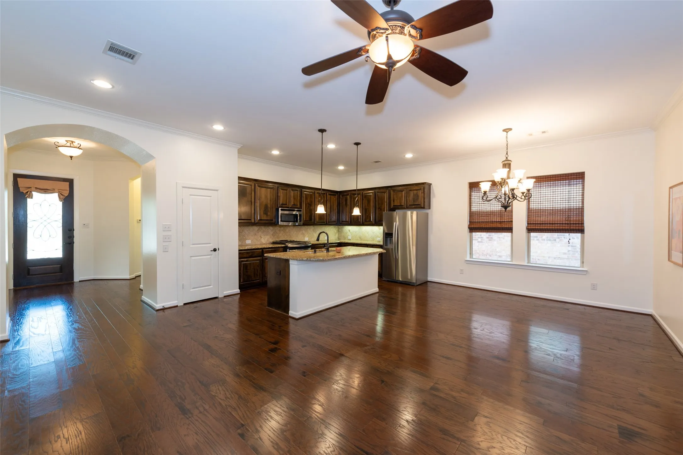 Open-concept living space featuring wood-finish flooring, a kitchen island with pendant lighting, stainless steel appliances, and a dining area with a chandelier