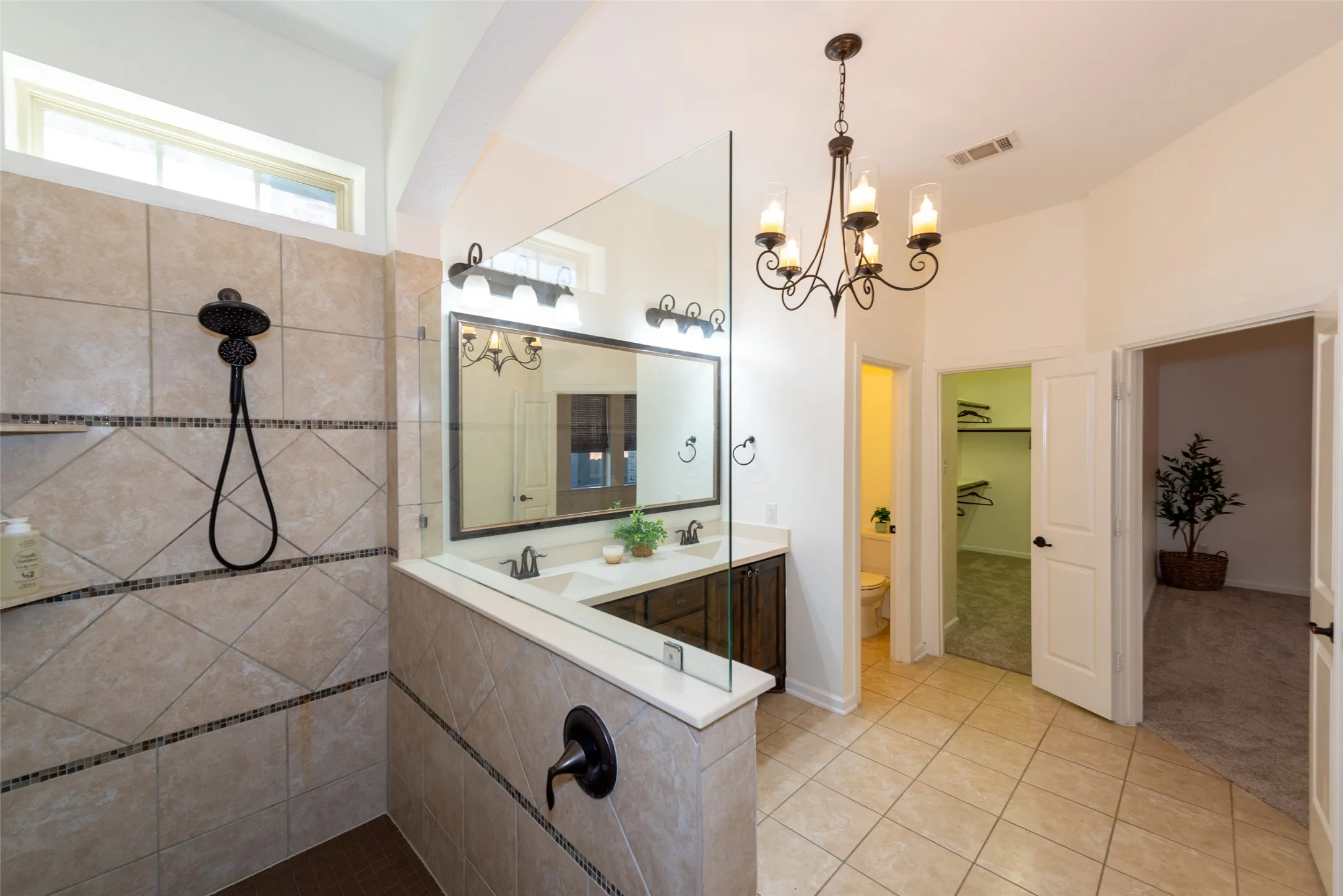 Spacious bathroom featuring a tile-surround shower with glass partition, dual vanity with undermount sinks, and a decorative chandelier