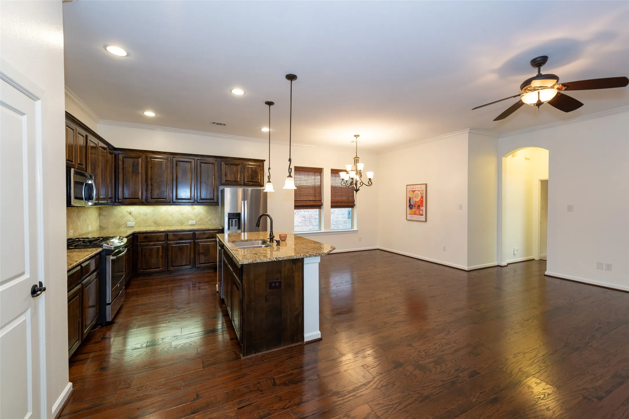 Open-concept living space featuring dark wood-finish flooring, a kitchen with dark cabinetry and stainless steel appliances, a kitchen island with pendant lighting, and recessed lighting throughout
