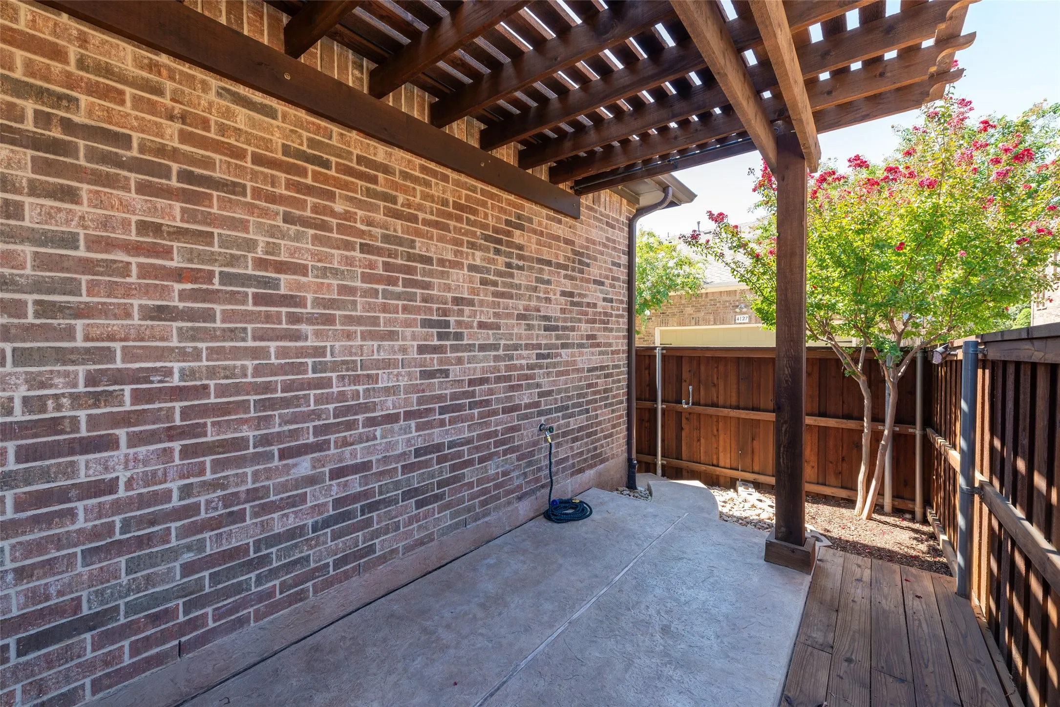 Outdoor patio featuring a wooden pergola, brick exterior wall, and concrete pad