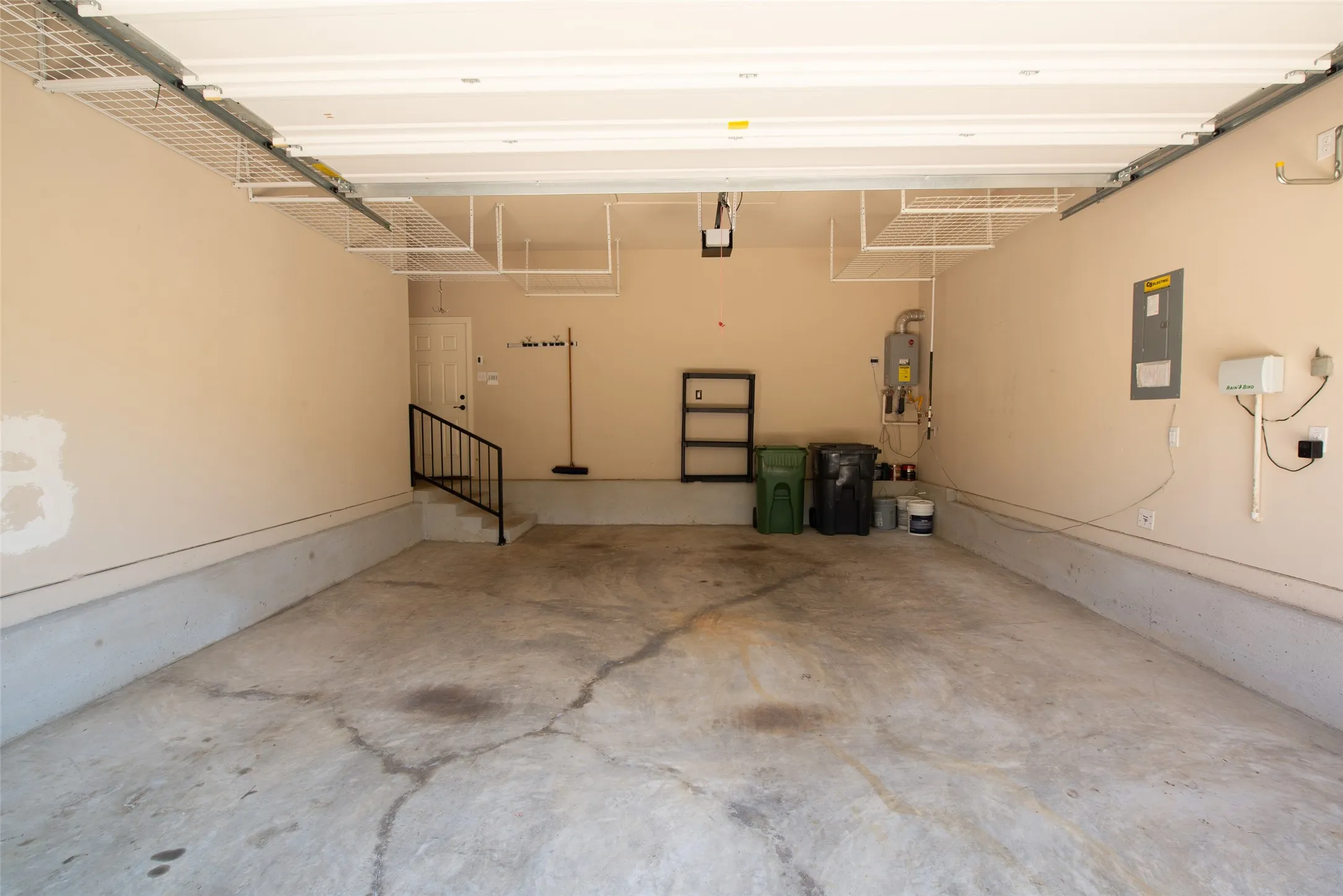 Spacious garage featuring overhead wire shelving, concrete flooring, and an interior access door with a black metal handrail