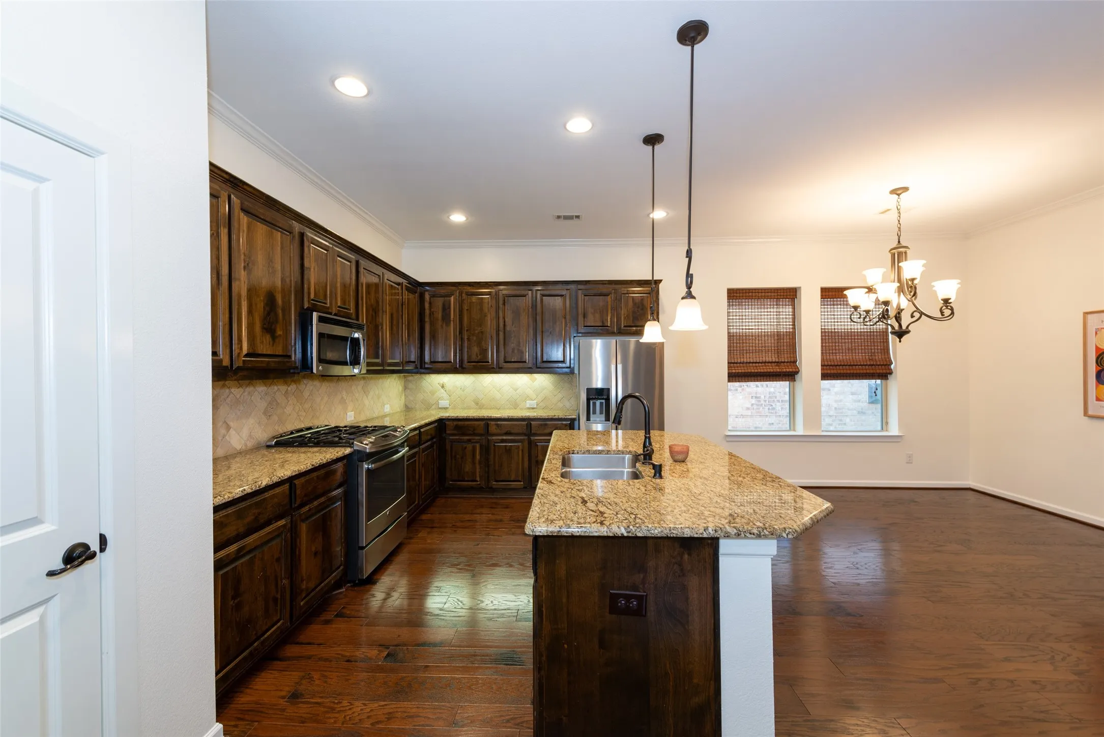 Gourmet kitchen with rich wood cabinetry, granite countertops, stainless steel appliances, a tile backsplash, and a central island with a built-in sink