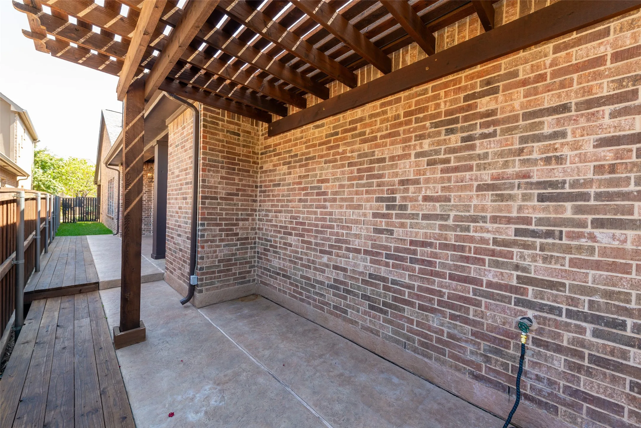 Patio area featuring a wood pergola, brick exterior, concrete flooring, and a wood plank walkway